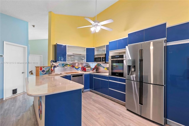 kitchen featuring high vaulted ceiling, a sink, blue cabinetry, stainless steel appliances, and a peninsula