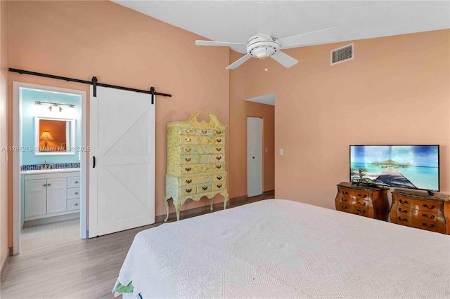 bedroom with visible vents, connected bathroom, lofted ceiling, a barn door, and wood finished floors