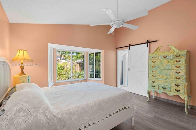 bedroom featuring a ceiling fan, wood finished floors, lofted ceiling, a textured ceiling, and a barn door