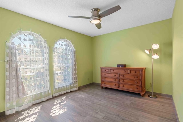 bedroom with a textured ceiling, a ceiling fan, baseboards, and wood finished floors