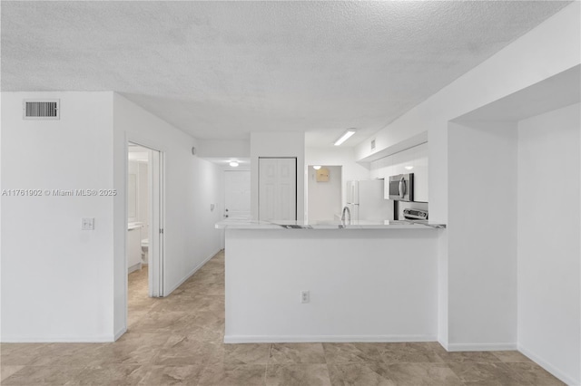 kitchen with visible vents, stainless steel microwave, white cabinetry, freestanding refrigerator, and a peninsula