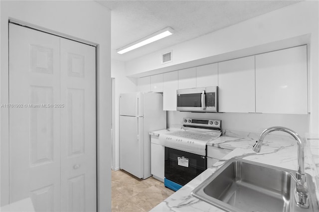 kitchen featuring freestanding refrigerator, a sink, stove, white cabinets, and stainless steel microwave