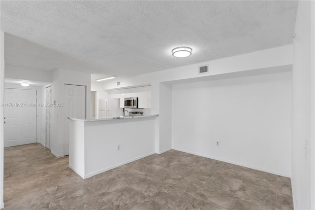 interior space with visible vents, stainless steel microwave, light countertops, freestanding refrigerator, and white cabinetry