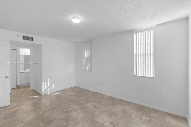 spare room with visible vents, a textured ceiling, and baseboards