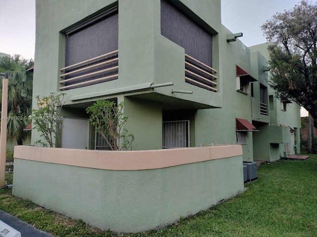 back of property with stucco siding, central air condition unit, and a lawn