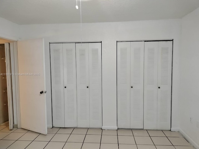 unfurnished bedroom featuring light tile patterned floors and two closets