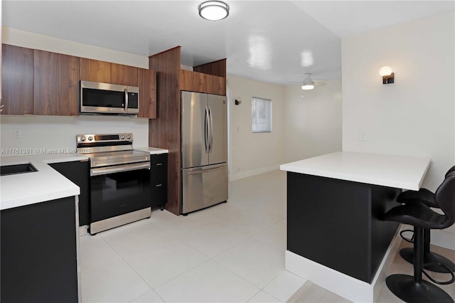 kitchen featuring a ceiling fan, a kitchen breakfast bar, stainless steel appliances, a peninsula, and light countertops