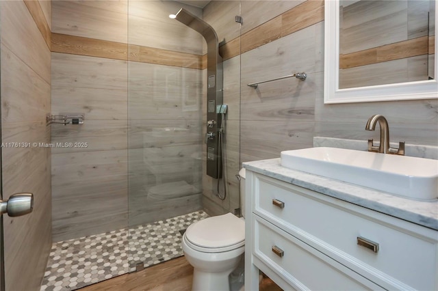 bathroom with toilet, a walk in shower, wood finished floors, tile walls, and vanity