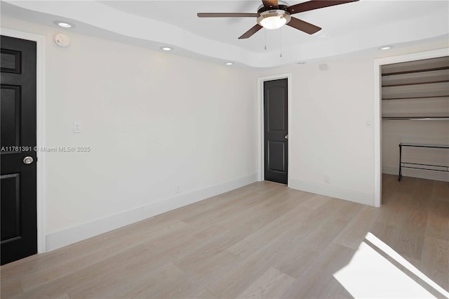 empty room featuring recessed lighting, baseboards, a raised ceiling, and wood finished floors