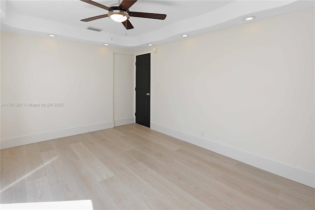 empty room with visible vents, baseboards, light wood-type flooring, a tray ceiling, and recessed lighting