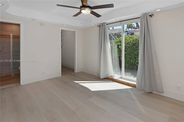 spare room featuring a tray ceiling, baseboards, and light wood finished floors