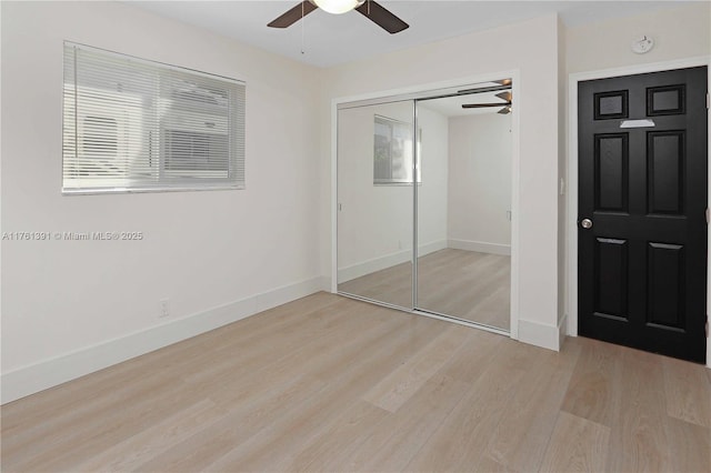 unfurnished bedroom featuring multiple windows, a closet, light wood finished floors, baseboards, and ceiling fan