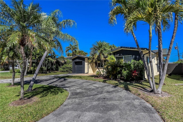 view of property hidden behind natural elements with stucco siding, a front lawn, driveway, and fence