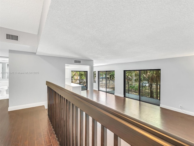 corridor with dark wood finished floors, baseboards, visible vents, and a textured ceiling