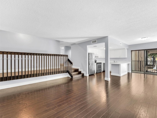 unfurnished living room featuring visible vents, baseboards, dark wood finished floors, stairway, and a sink