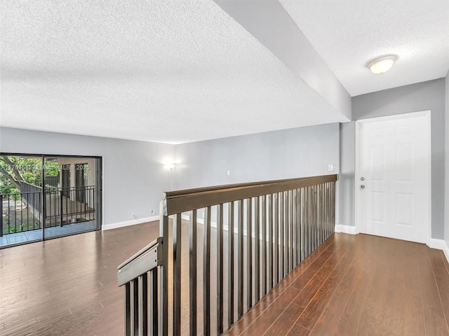 hallway with baseboards, a textured ceiling, and wood finished floors