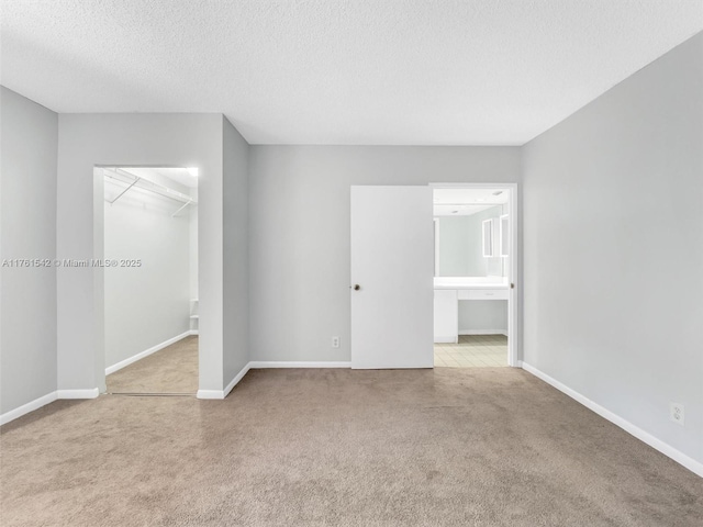 unfurnished bedroom with a walk in closet, carpet flooring, baseboards, and a textured ceiling