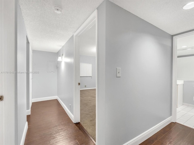 corridor with baseboards, dark wood-style flooring, and a textured ceiling