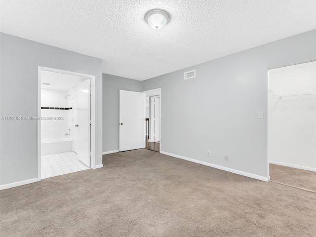 unfurnished bedroom with visible vents, carpet flooring, a closet, a textured ceiling, and ensuite bath