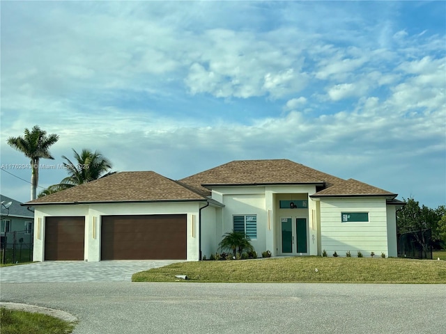 view of front of house with decorative driveway, french doors, a front yard, a shingled roof, and a garage