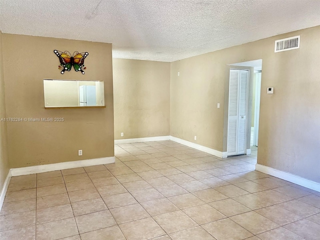 spare room featuring light tile patterned floors, baseboards, visible vents, and a textured ceiling