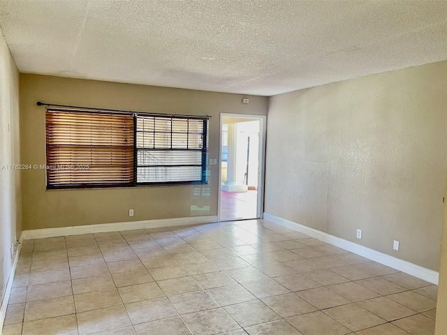 spare room with light tile patterned flooring, a textured ceiling, and baseboards