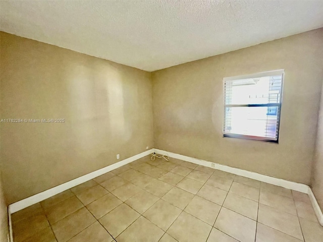 unfurnished room featuring light tile patterned floors, a textured ceiling, and baseboards