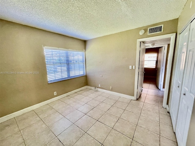 unfurnished room featuring light tile patterned floors, visible vents, a textured ceiling, and baseboards