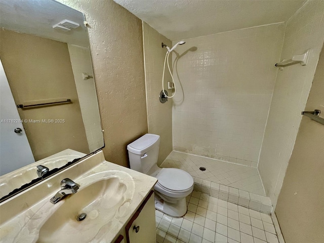 bathroom with a tile shower, toilet, vanity, and a textured wall