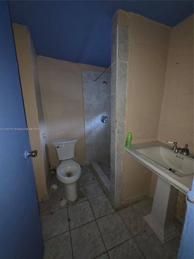 bathroom featuring tile patterned flooring, toilet, and a tile shower