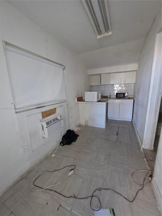 kitchen with a wall mounted air conditioner, backsplash, white cabinets, black microwave, and white microwave