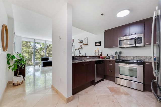 kitchen with light tile patterned floors, light stone countertops, stainless steel appliances, and a sink