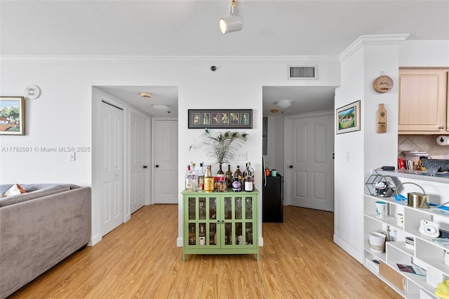 interior space with light wood-style floors, visible vents, backsplash, and ornamental molding