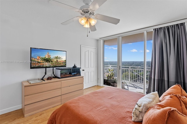 bedroom with a ceiling fan, light wood-style floors, a wall of windows, baseboards, and access to exterior