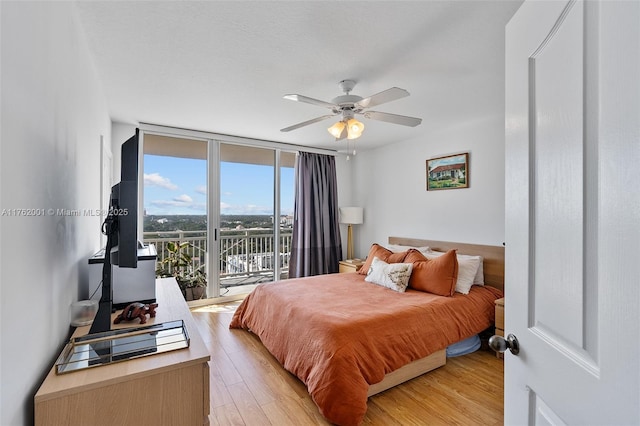 bedroom featuring a ceiling fan, a wall of windows, light wood-style floors, and access to outside