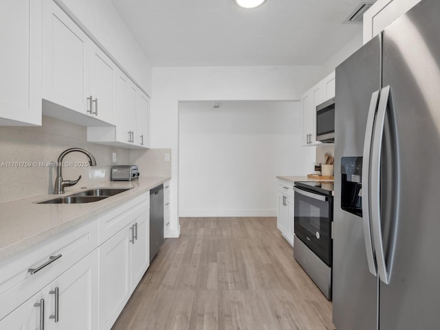 kitchen with white cabinetry, stainless steel appliances, light wood-style floors, and a sink