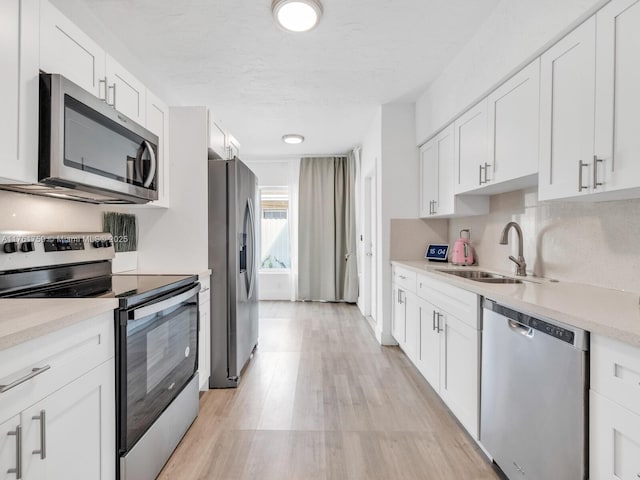 kitchen with light wood finished floors, light countertops, stainless steel appliances, white cabinetry, and a sink