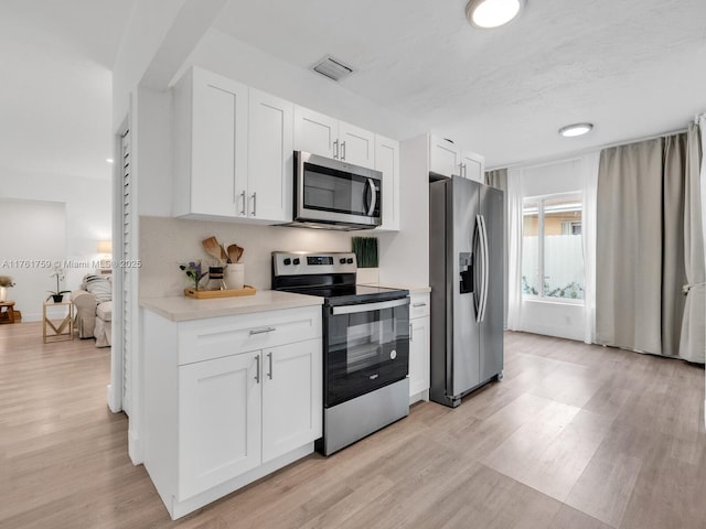 kitchen with visible vents, stainless steel appliances, light countertops, white cabinets, and light wood-style floors