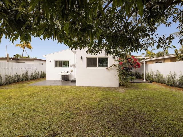 rear view of house with stucco siding, a yard, a fenced backyard, and a patio area