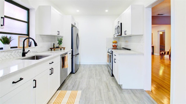 kitchen with a sink, backsplash, appliances with stainless steel finishes, and white cabinetry