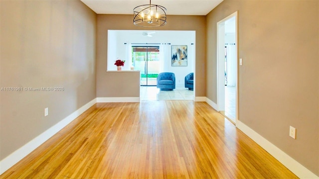 empty room featuring baseboards, an inviting chandelier, and light wood finished floors