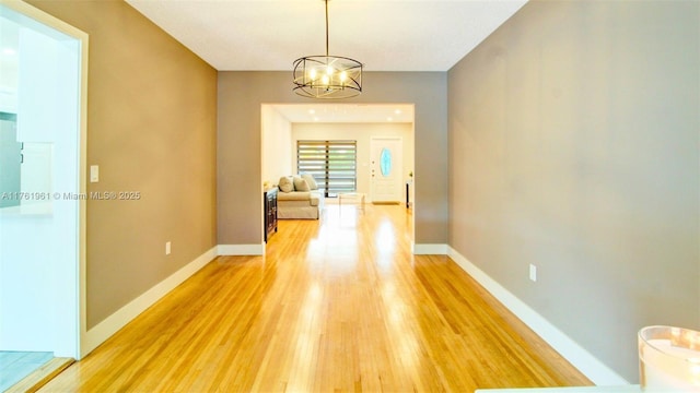 corridor featuring baseboards, a notable chandelier, and light wood-style flooring