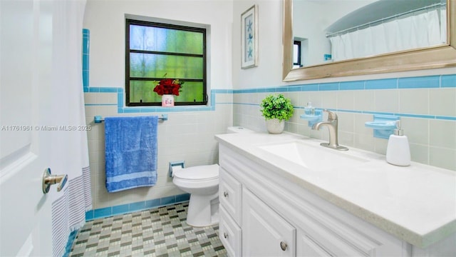 full bath featuring tile patterned flooring, a wainscoted wall, toilet, vanity, and tile walls