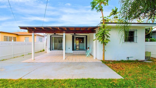 rear view of property featuring stucco siding, a patio, a ceiling fan, and fence