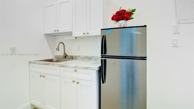 kitchen featuring electric panel, white cabinets, freestanding refrigerator, and a sink