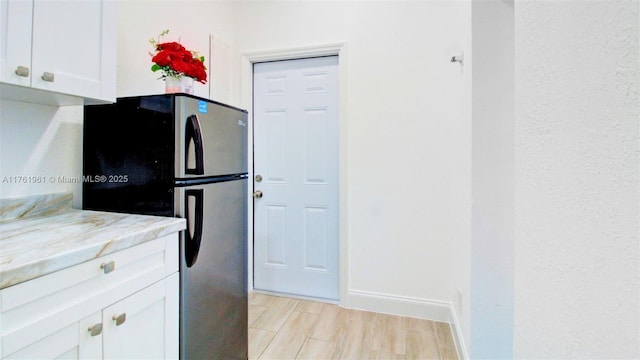 kitchen with baseboards, light stone counters, light wood-style flooring, freestanding refrigerator, and white cabinetry