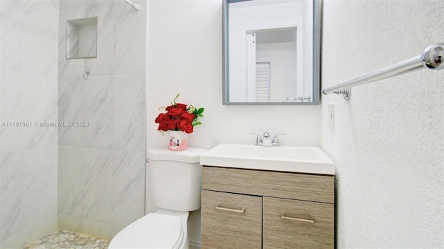 bathroom with toilet, vanity, and a tile shower