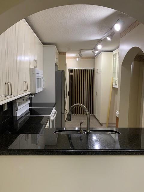 kitchen with range with electric cooktop, a textured ceiling, freestanding refrigerator, dark stone counters, and white microwave