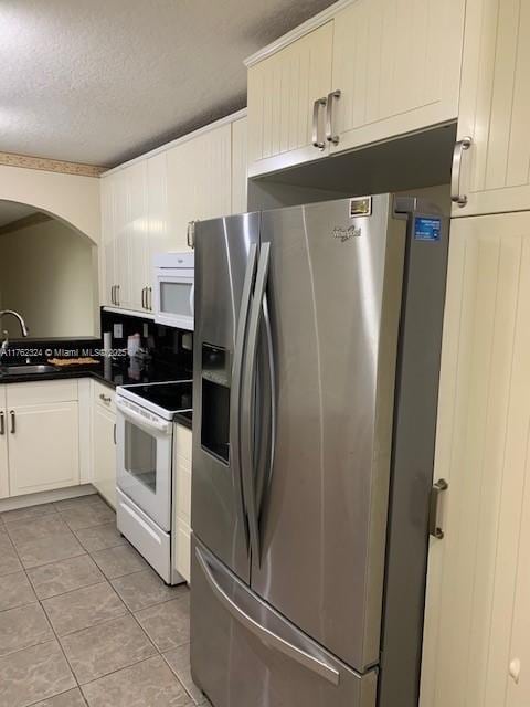 kitchen featuring dark countertops, light tile patterned floors, white range with electric stovetop, stainless steel fridge, and a sink