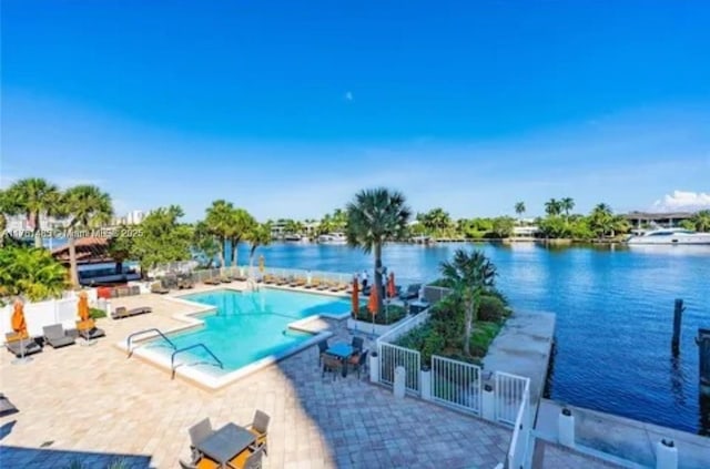 pool with a patio area, a water view, and fence